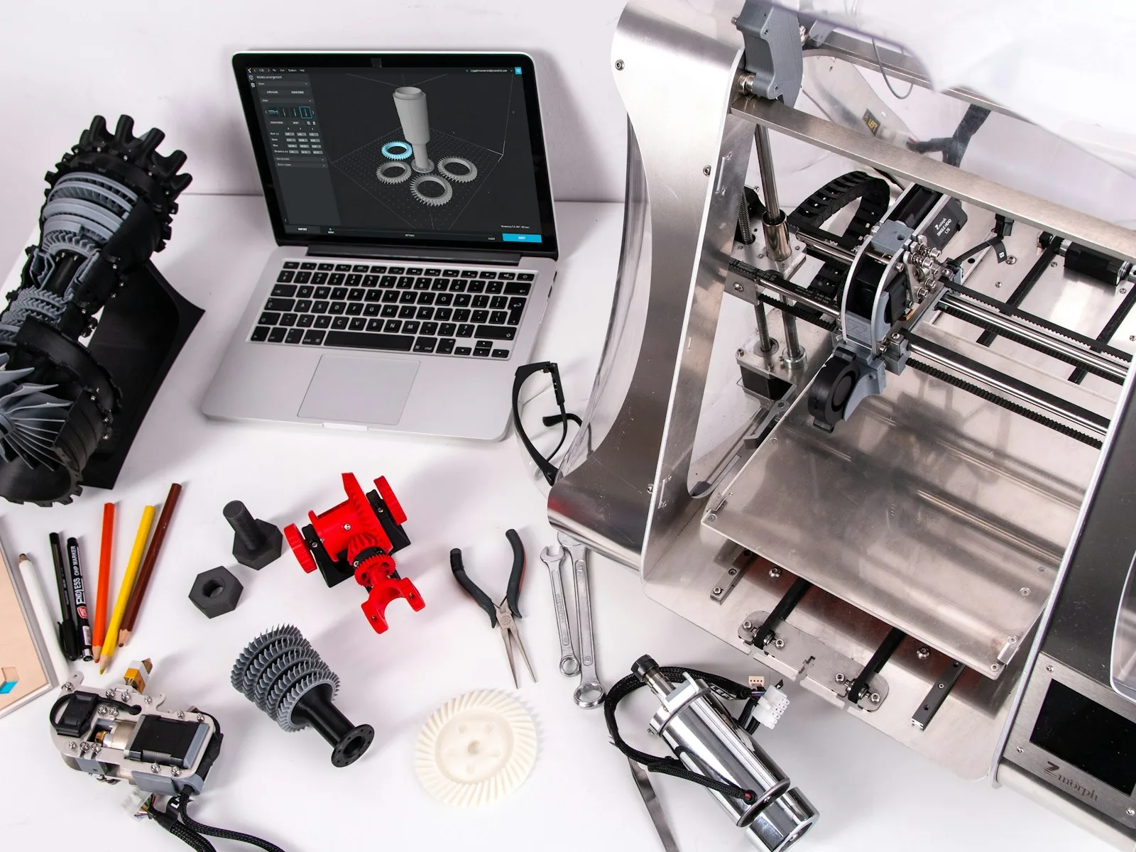 Arbeitsplatz mit digitalem 3D-Modell, Bauteilen und einem 3D-Drucker.