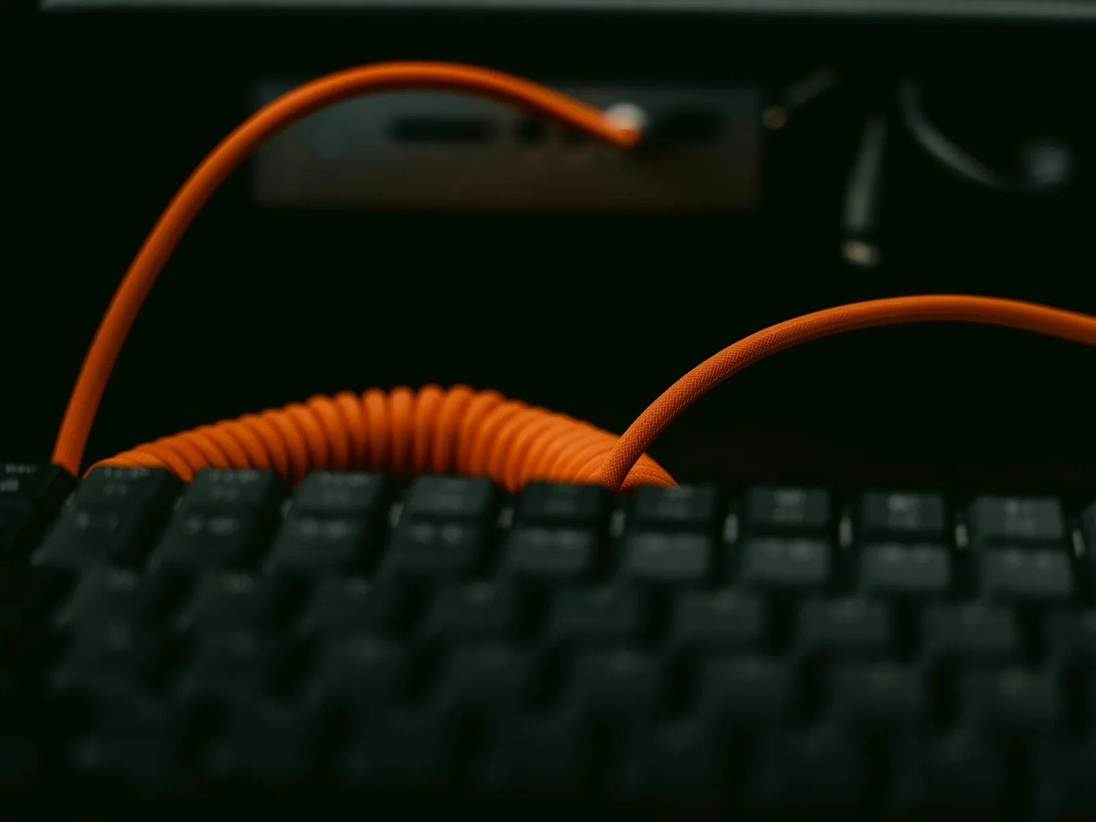 A mechanical keyboard with an orange cable on a dark work surface.