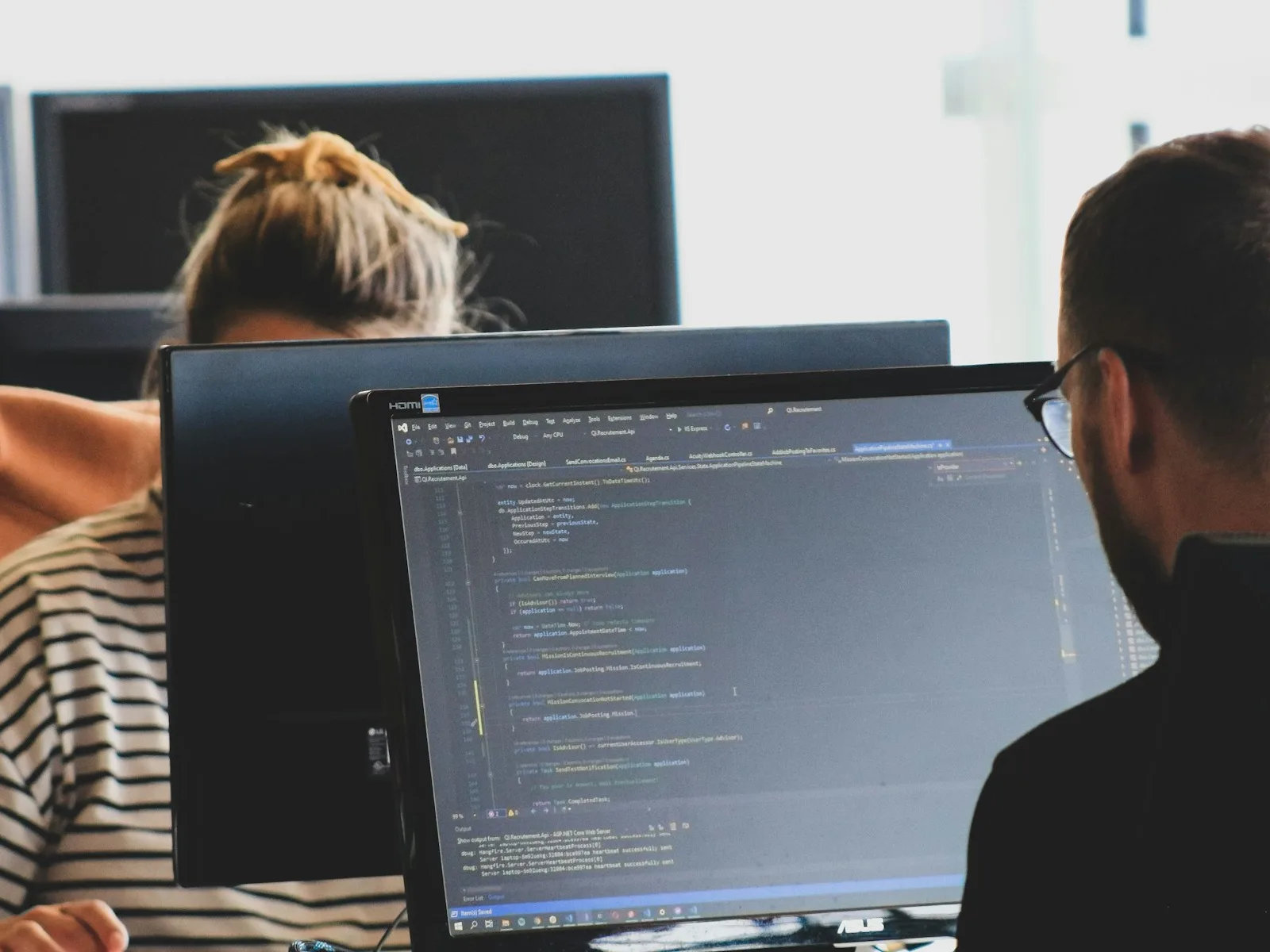 Zwei Personen prüfen Quellcode an Monitoren in einer Entwicklungsumgebung.