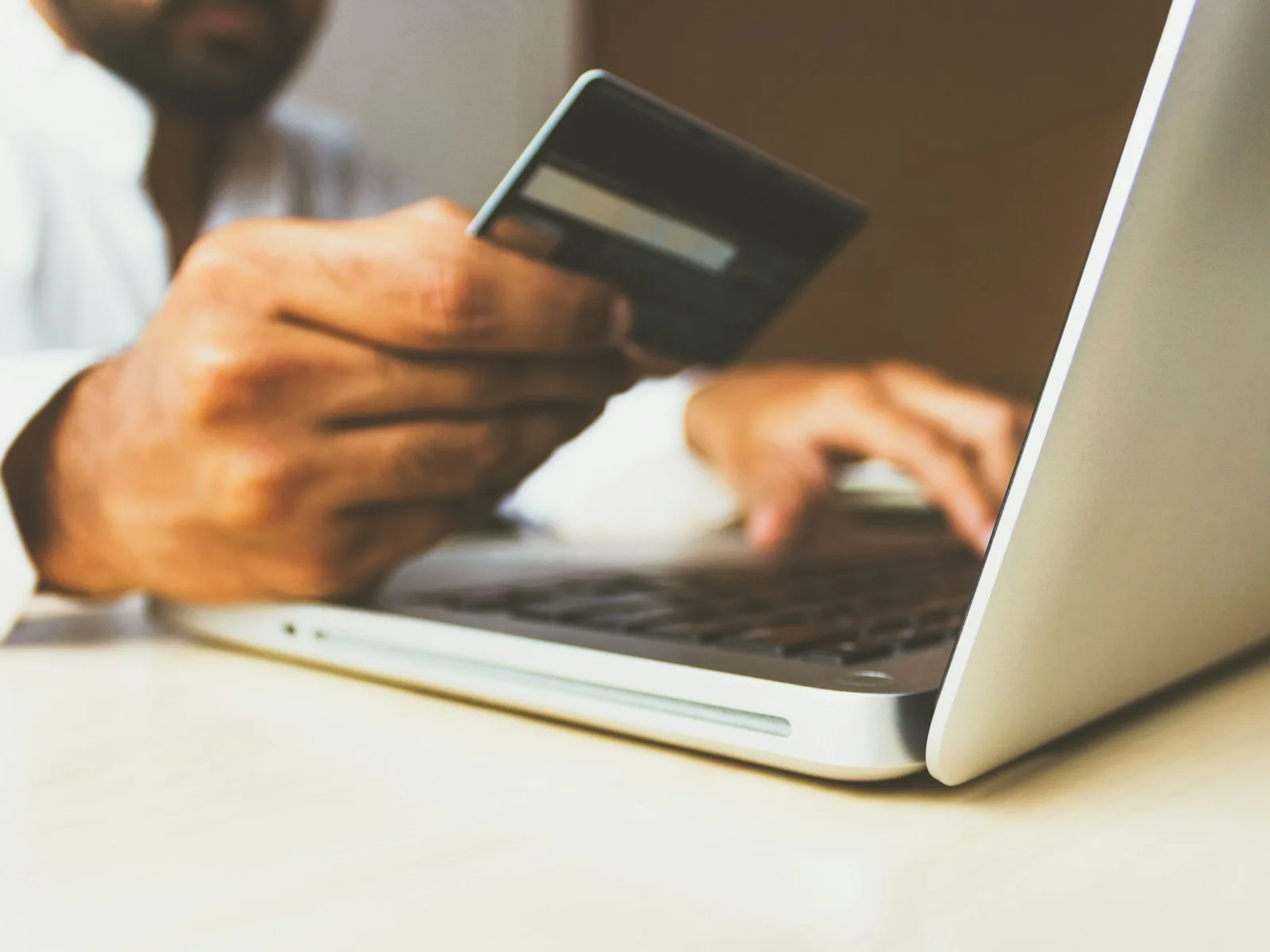 Hand mit Zahlungskarte neben einer geöffneten Shopseite auf dem Laptop.