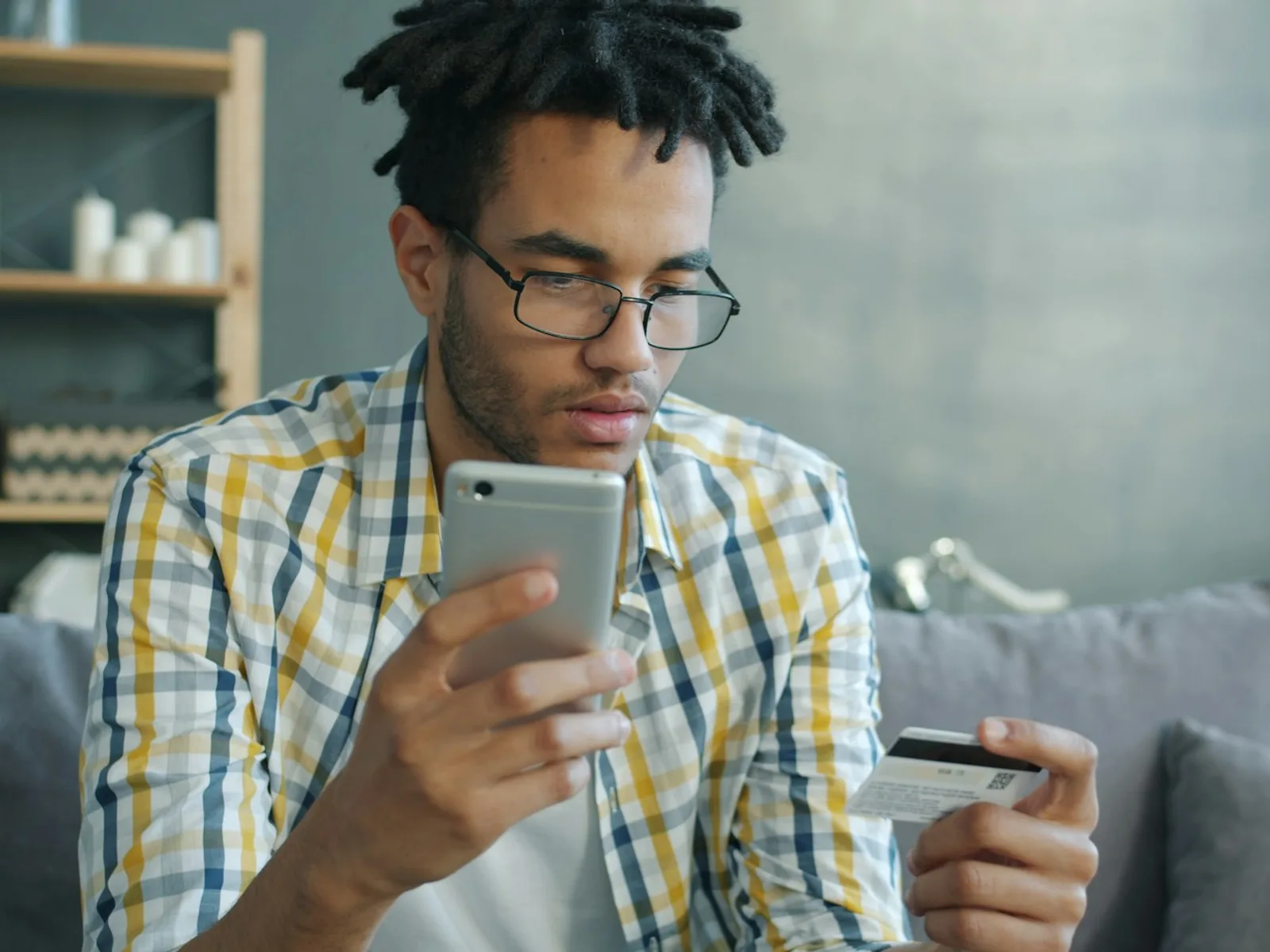 Person vergleicht Angaben auf dem Smartphone und hält eine Zahlungskarte bereit.