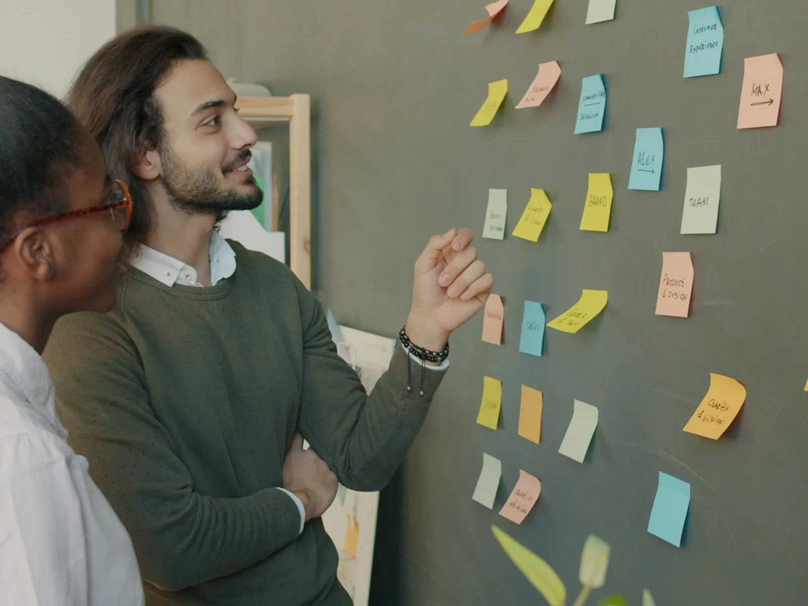 Zwei Personen besprechen und ordnen Notizen an einer Wand.