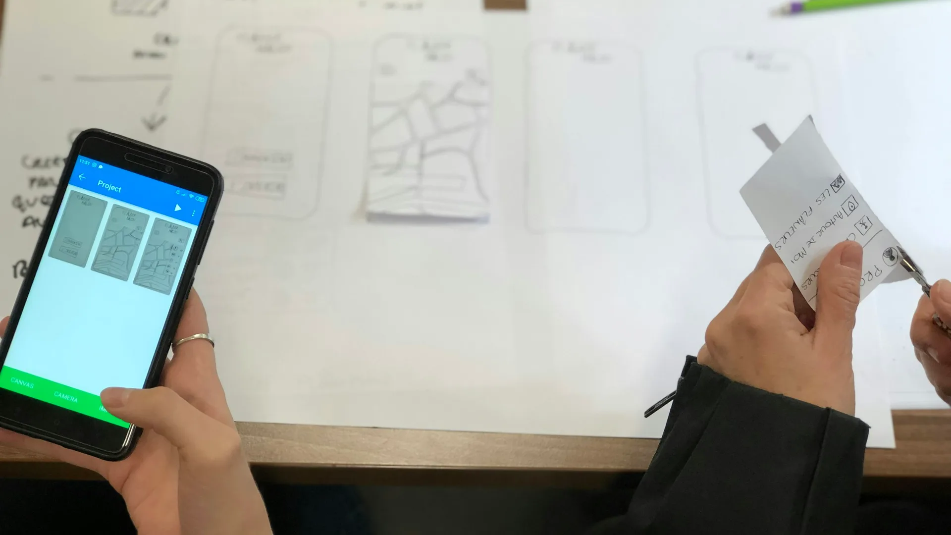 Hände arbeiten mit ausgeschnittenen Bildschirm-Skizzen und einem Prototyp auf dem Smartphone.